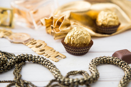 妇女组的配件和糖果在金色木制背景 香水 糖果 巧克力 手表 珠宝 金袋。复制 space.selective 焦点