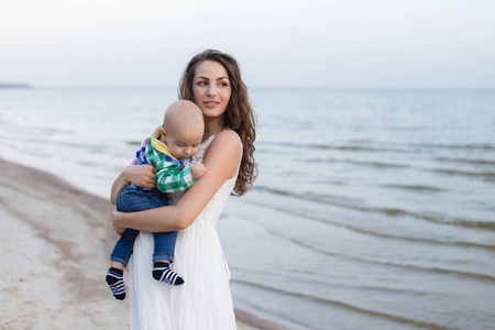 年轻的母亲，她在海边沙滩上的怀里抱着一个婴儿