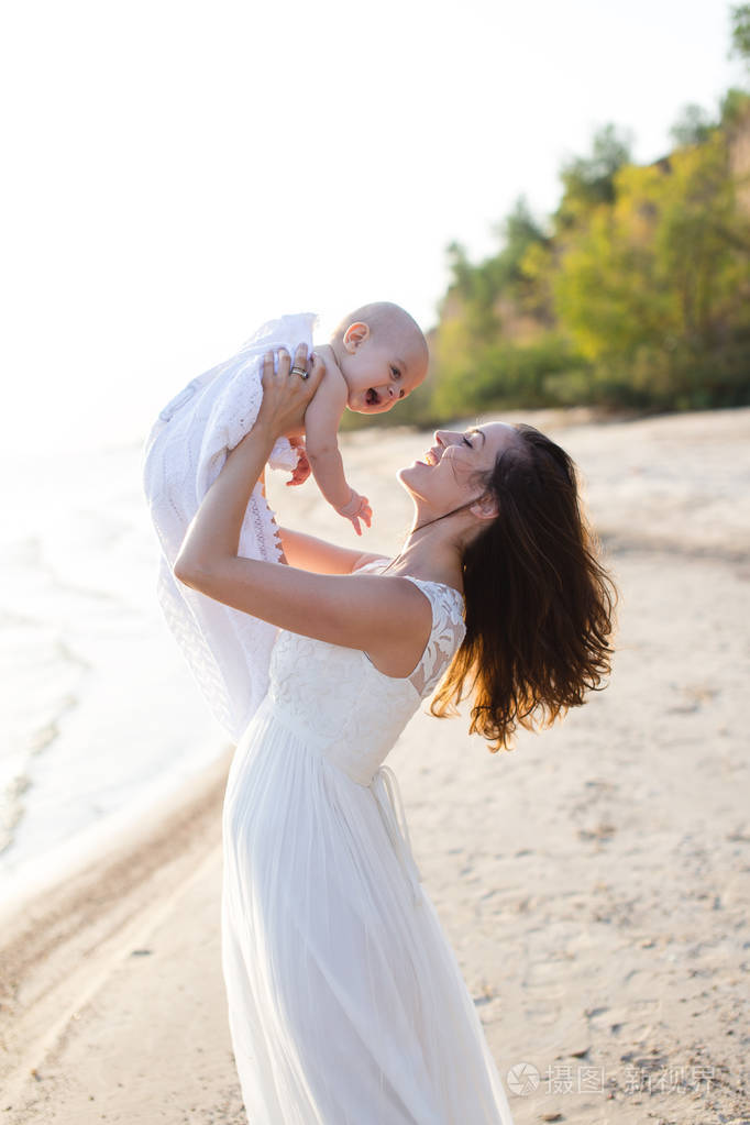 年轻的母亲她在海边沙滩上的怀里抱着一个婴儿
