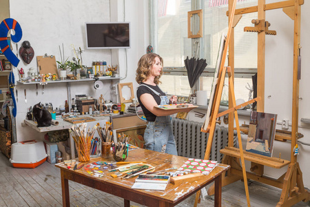 创意和休闲理念-女学生或女青年艺术家,画架,调色板和画笔在画室画画