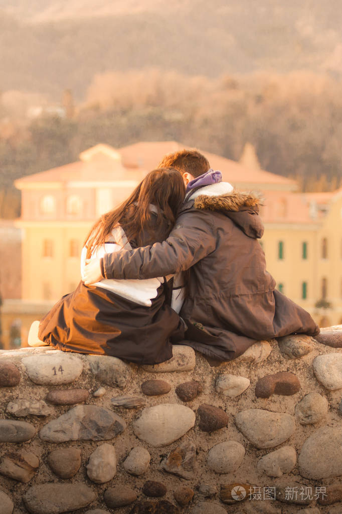 亲吻情人节那天日落时分坐在一堵墙上的恋爱中的男孩