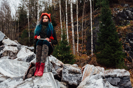 艺术家画坐在悬崖上，岩石上的女孩记事本。美好的秋天视图