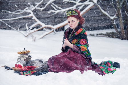 在苹果与茶炊一冬天下雪天强的霜的俄罗斯风格的华丽年轻女子肖像连买衣服。在传统头饰女俄罗斯模特