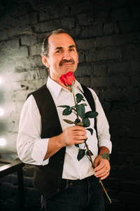 英俊的中间位老人穿着一件白衬衫和黑色的背心，拿着红色的玫瑰花，学士。黑色背景