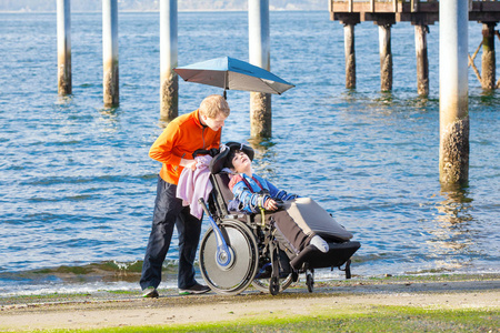 与他在海滩上的照顾坐轮椅的残疾的男孩