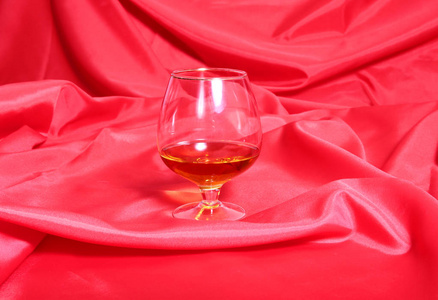 白陶瓷杯的咖啡和白兰地酒，一副眼镜，果仁糖红色背景上