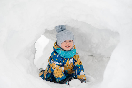 可爱的小男孩孩子在外面玩，他在堆雪挖在冬天里的雪屋堡隧道