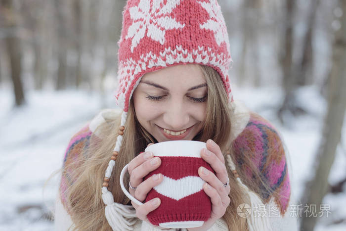 冬天的女人抱着一大杯暖和暖和身子。可爱的年轻女人喝酒茶或咖啡户外