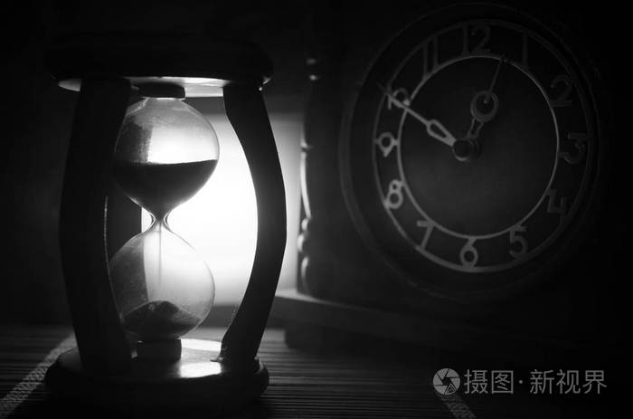 时间概念沙漏钟和老复古木时钟的剪影与箭头和烟在黑暗的背景与热的