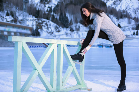 漂亮的女人滑冰冬季户外，穿溜冰鞋。在背景中的山