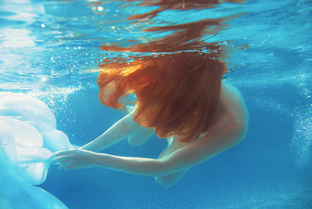 年轻漂亮的红头发女孩水下游泳池在夏天，白色的衣服里的肖像