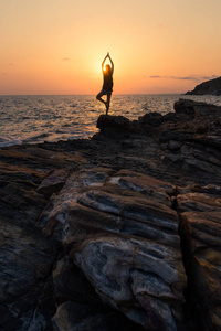 剪影年轻女人上练瑜伽的岩石在日落时分，Ra