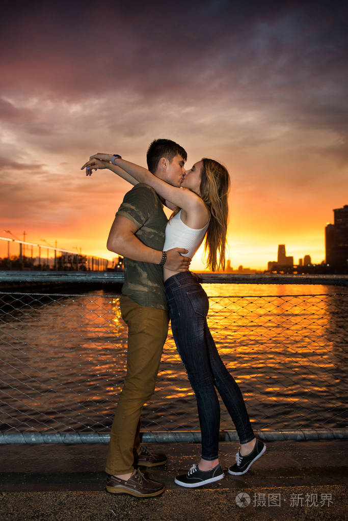 在日落的时候在市海洋码头附近的年轻美丽的夫妇在爱接吻