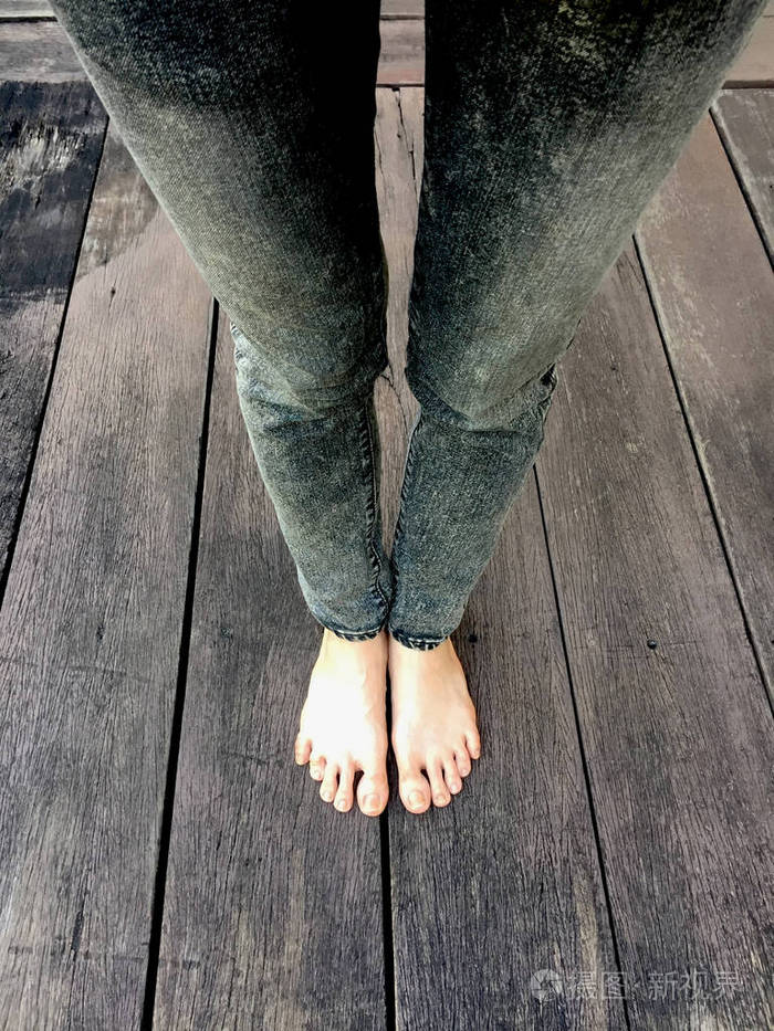 女人的牛仔裤赤着脚上的木制的背景