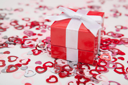 与彩色心五彩纸屑在白色背景上的红色礼品盒。情人节贺卡