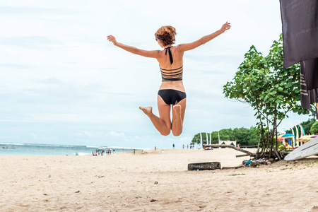 美丽少妇在热带巴厘岛，印度尼西亚的海滩上跳跃为喜悦。阳光灿烂的夏天一天现场