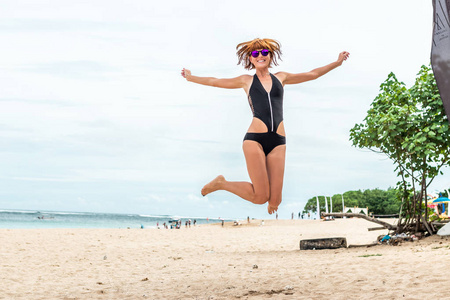 美丽少妇在热带巴厘岛，印度尼西亚的海滩上跳跃为喜悦。阳光灿烂的夏天一天现场