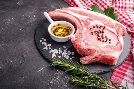 在深色背景上的生肉。生猪肉牛排配香草 油和香料。烹饪的肉