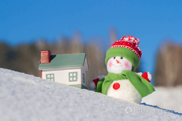 雪人站在旁边的雪坡上的房子.蓝蓝的天空.冬天背景