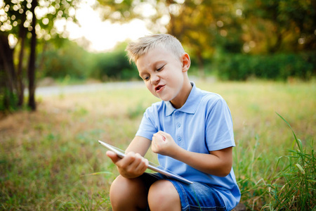 年轻的孩子坐在院子里和 tablet pc 上玩游戏