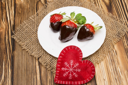 新鲜草莓蘸上黑巧克力和木制背景上的心。情人节那天