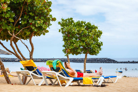 身份不明的男子在用手机在沙滩的躺椅上