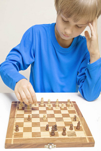 一个小的白人男孩玩象棋和制作的下一步行动的肖像