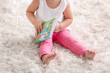 可爱的小女孩坐在地毯上拿着本书，特写