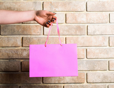 在砖墙上的女性手中的粉色购物袋。