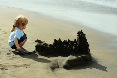 可爱的小宝贝男孩建立在沙滩上的堆沙堡