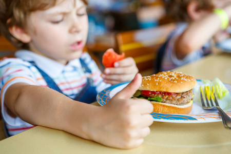 可爱健康学龄前孩子吃汉堡包坐在学校的食堂