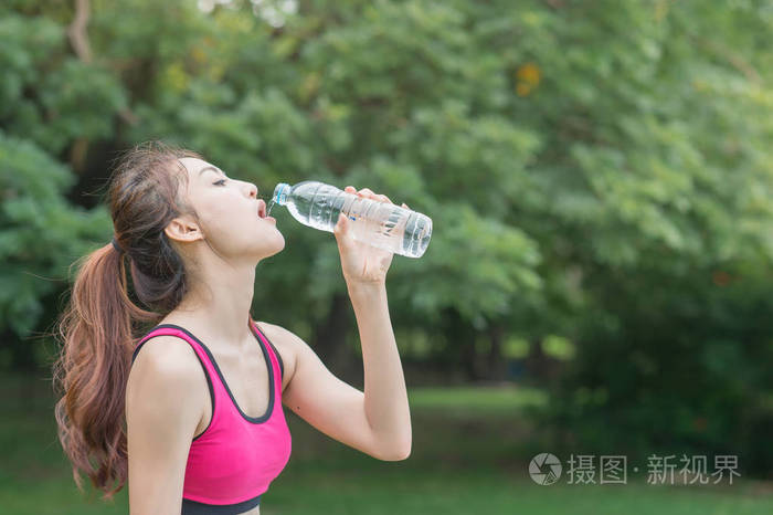 从塑料瓶在公园里年轻有魅力的女人喝水