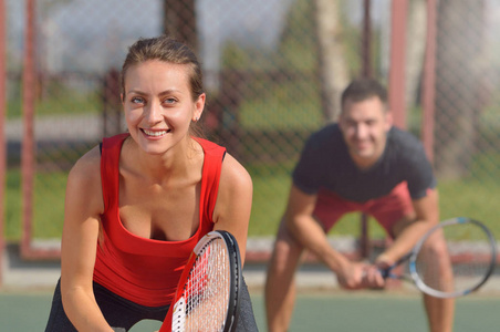 在网球场夫妇打双打。微笑的女士在第一架飞机