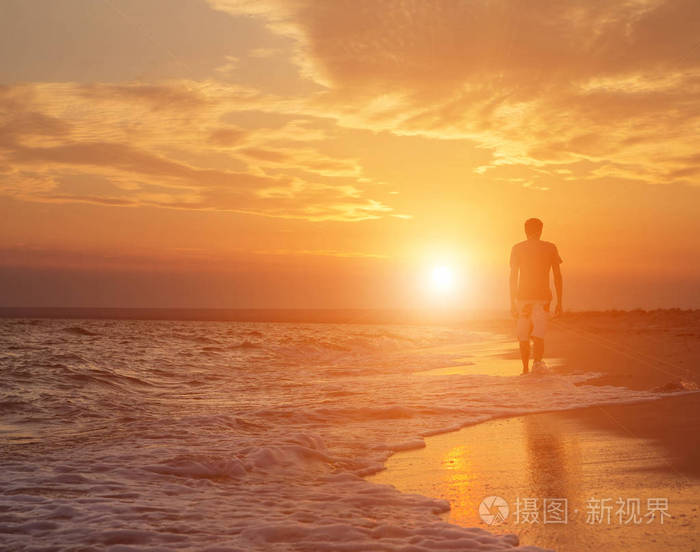 一个年轻男子在海滩上散步的剪影在一个美丽的日落的背景下