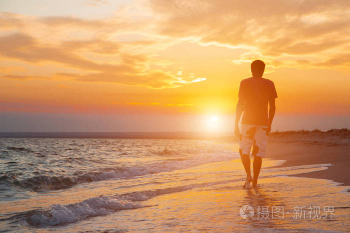 一个年轻男子在海滩上散步的剪影在一个美丽的日落的背景下