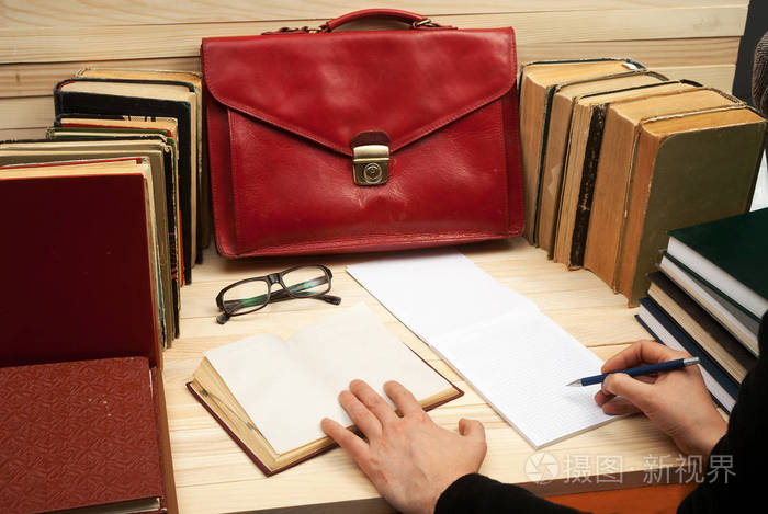 专业律师坐在桌前和文件上签字.上一张木桌书籍,文档,眼镜,红色公文包