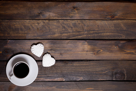 白色大杯咖啡和两颗棉花糖在一个木制的背景上的心的形状