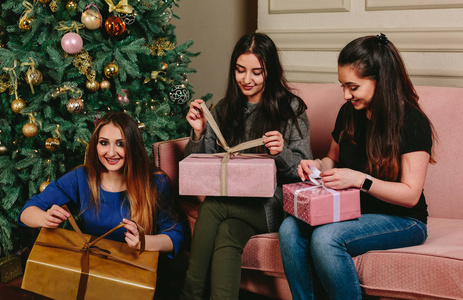 三个年轻漂亮的女孩解压礼物附近一棵圣诞树。工作室水平的肖像