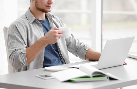 英俊的年轻男子，笔记本电脑上工作，在家里喝咖啡