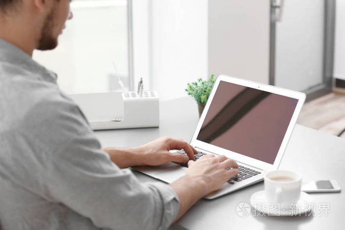 英俊的年轻男子,笔记本电脑上工作,在家里喝咖啡