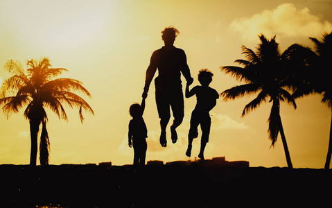 父亲与小儿子和女儿跳跃在日落海滩