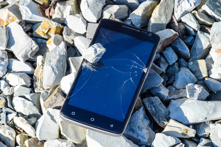 岩石上的沮丧电话。 智能手机上的玻璃碎在岩石上。 智能手机掉了下来。