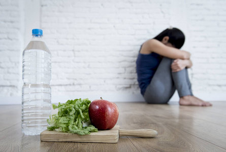 女人或十几岁的女孩坐在地面独自一人在家里担心遭受营养饮食失调症