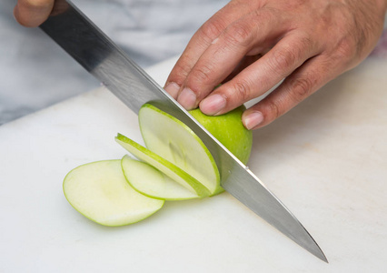 一把刀切薄片的新鲜有机绿色苹果，在一个白色的切割板上。