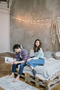 年轻的时髦夫妇阅读杂志与梦想手工制作床上