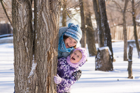 妈妈带小女儿从冬季的森林里的一棵树后面偷看
