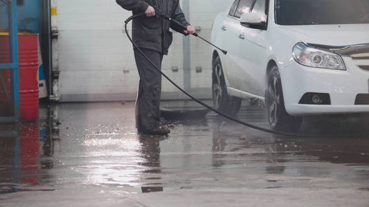 汽车服务的工人正在洗一辆车在肥皂水中的由水软管
