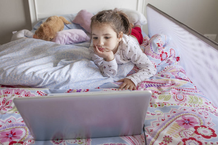 看电影用一台笔记本电脑在床上的小女孩