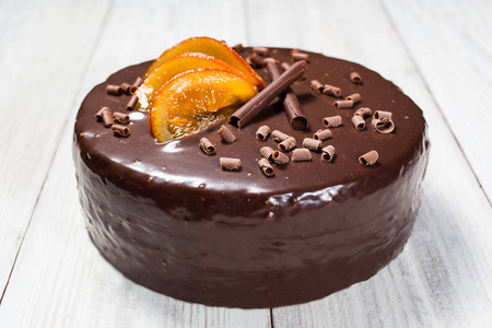 巧克力蛋糕蜜饯的橙子，巧克力蛋糕切的一块与叶片上灰色的背景，特写，黑巧克力蛋糕，美味素食巧克力蛋糕，美味的巧克力蛋糕上木制背景