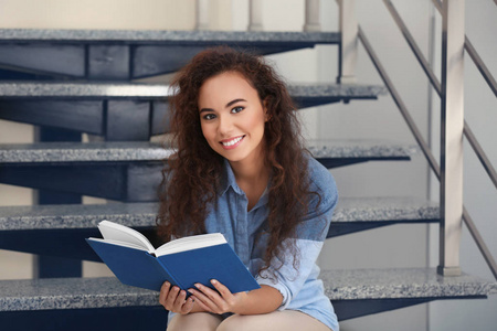 美丽的年轻女子坐在楼梯上，阅读本书
